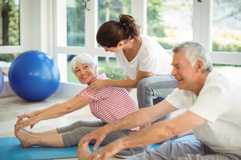 Female trainer assisting senior couple in performing exercise at home